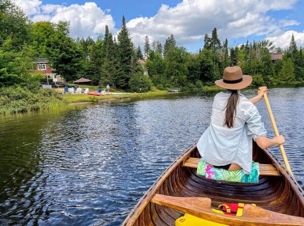 A person in a canoe on a river with houses and trees in the background.