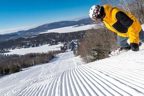 A snowboarder on a snowy slope with a clear view of a town and mountains in the background.