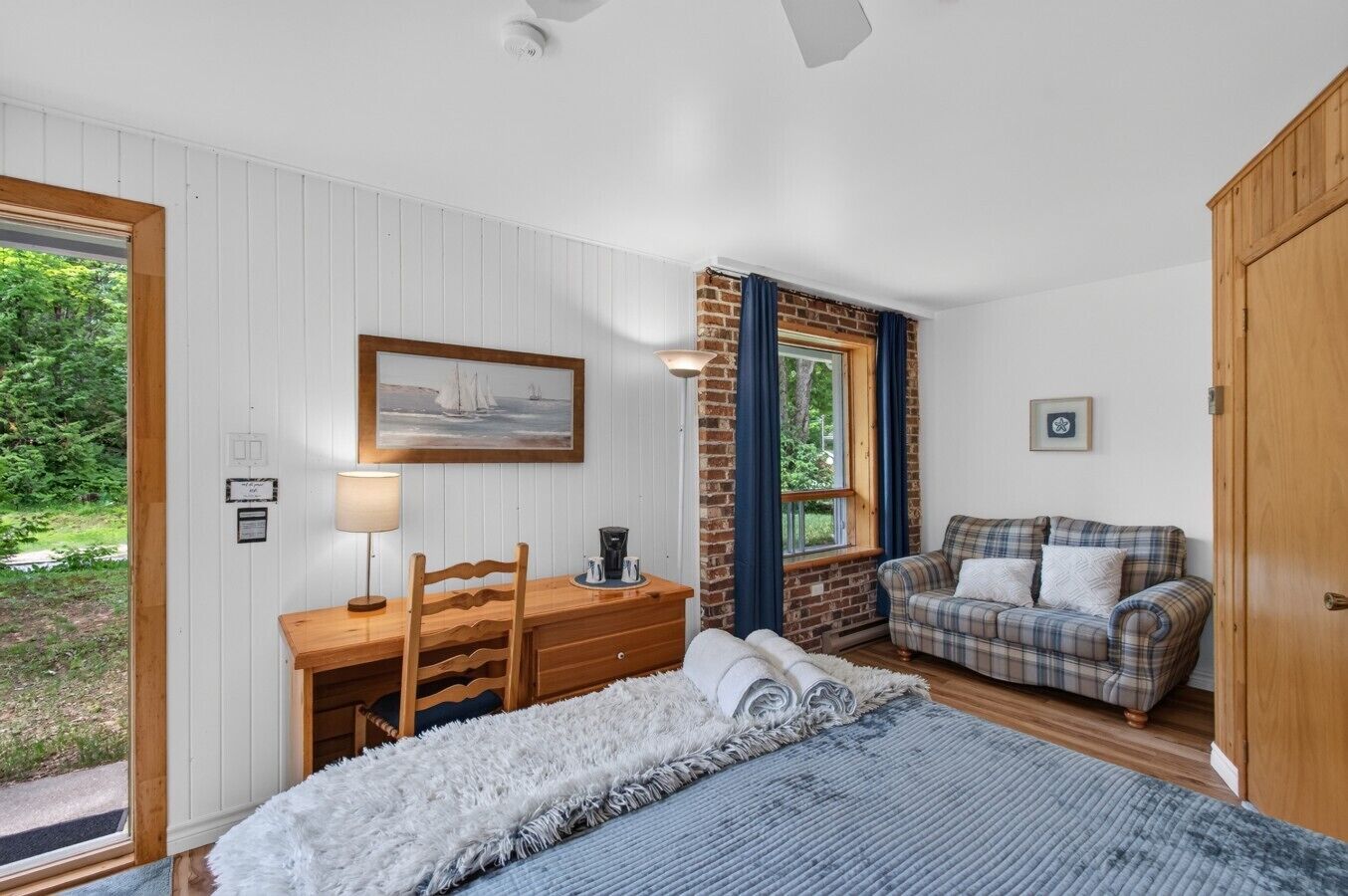 A bedroom with a bed, a desk, a chair, a plaid sofa, and a window with curtains.