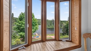 Una habitación con un ventanal grande de madera que da a un lago y un bosque.