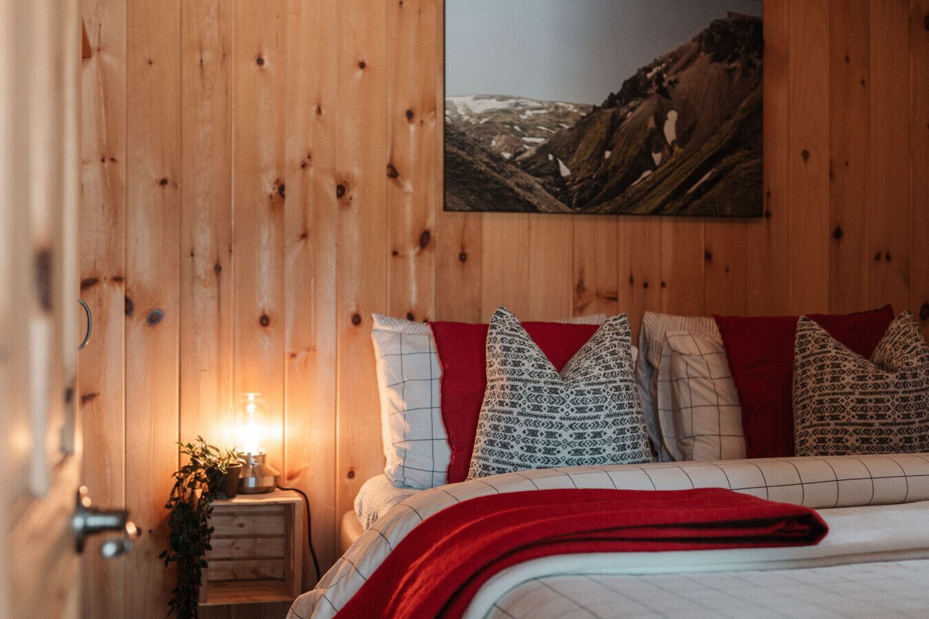 Una habitación con paneles de madera, una cama, almohadas, una mesita de noche y un cuadro colgado en la pared.