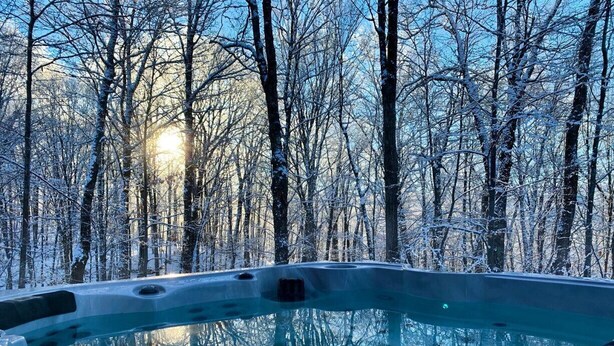 A hot tub surrounded by snow-covered trees with a clear sky.