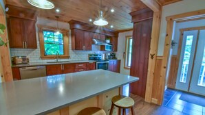 A kitchen with wooden cabinets, a large island with stools, a built-in oven, and a window with a view of greenery.