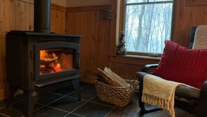 A cozy room with a wood-burning stove, a wicker basket, and a chair with a red cushion.