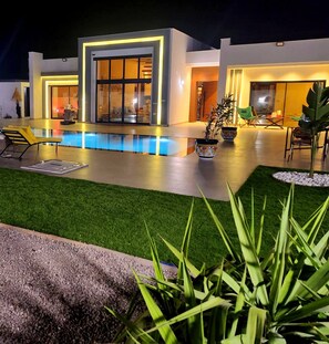 Une maison moderne dotée d’une piscine, d’un espace salon extérieur et d’une pelouse bien entretenue.