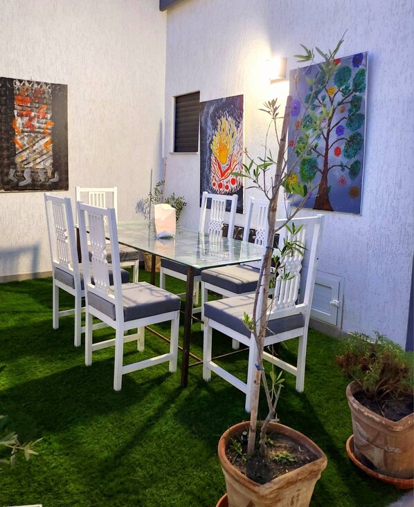 A dining area with a glass table and white chairs, surrounded by a small lawn and potted plants. - Room in B&B - Dar Tralala, Djerba Master Suite (Aghir)