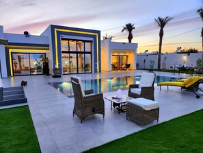Une maison moderne dotée d’une piscine, d’un espace salon extérieur et d’une pelouse bien entretenue.