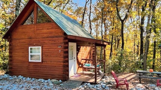 Une petite cabane en bois avec un toit en métal, une véranda avec un banc et une porte.