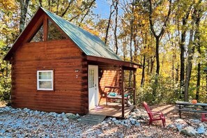 Eine kleine Holzhütte mit einem Metalldach, einer Veranda mit einer Bank und einer Tür.