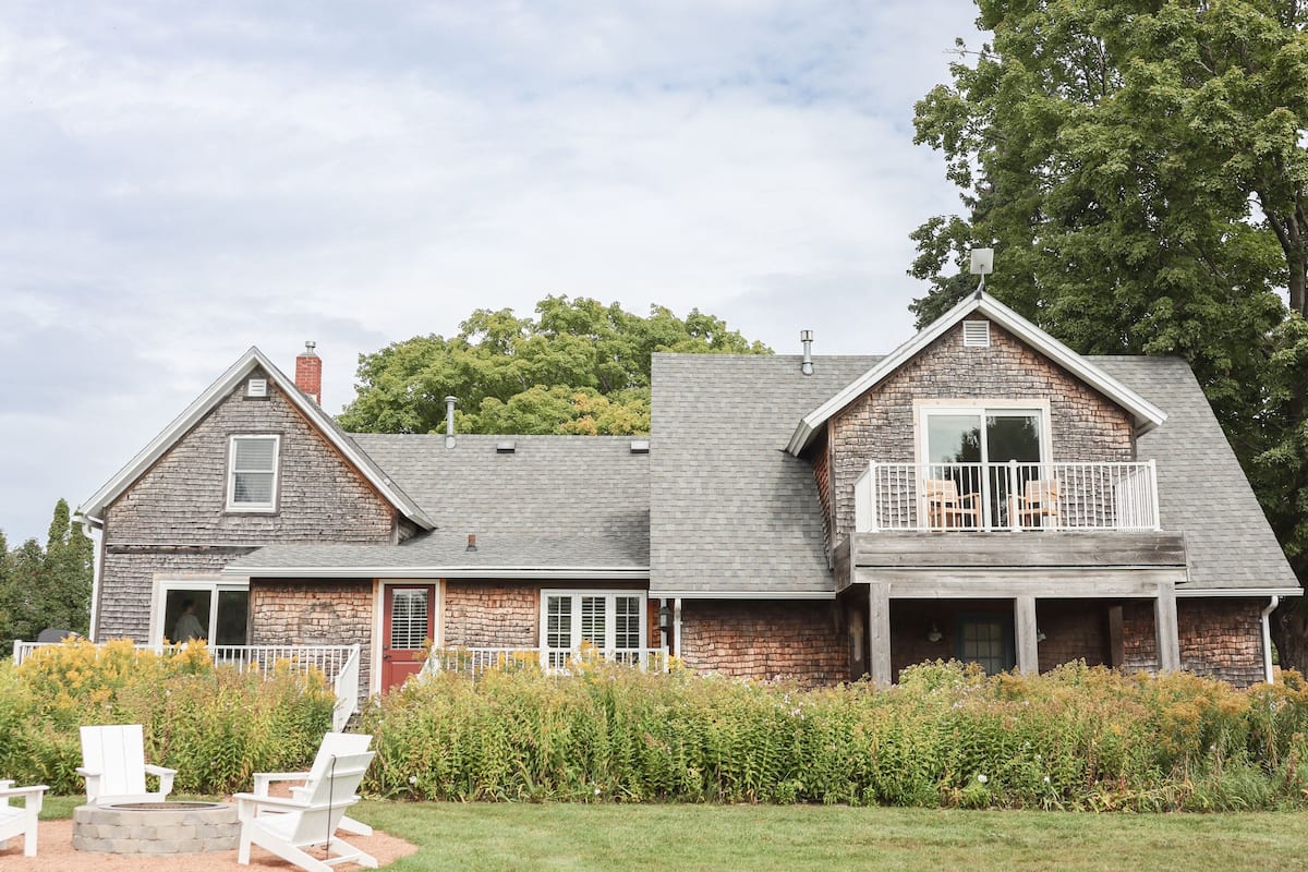 A two-story house with a stone facade, a balcony with white railings, and a fire pit area with white chairs.