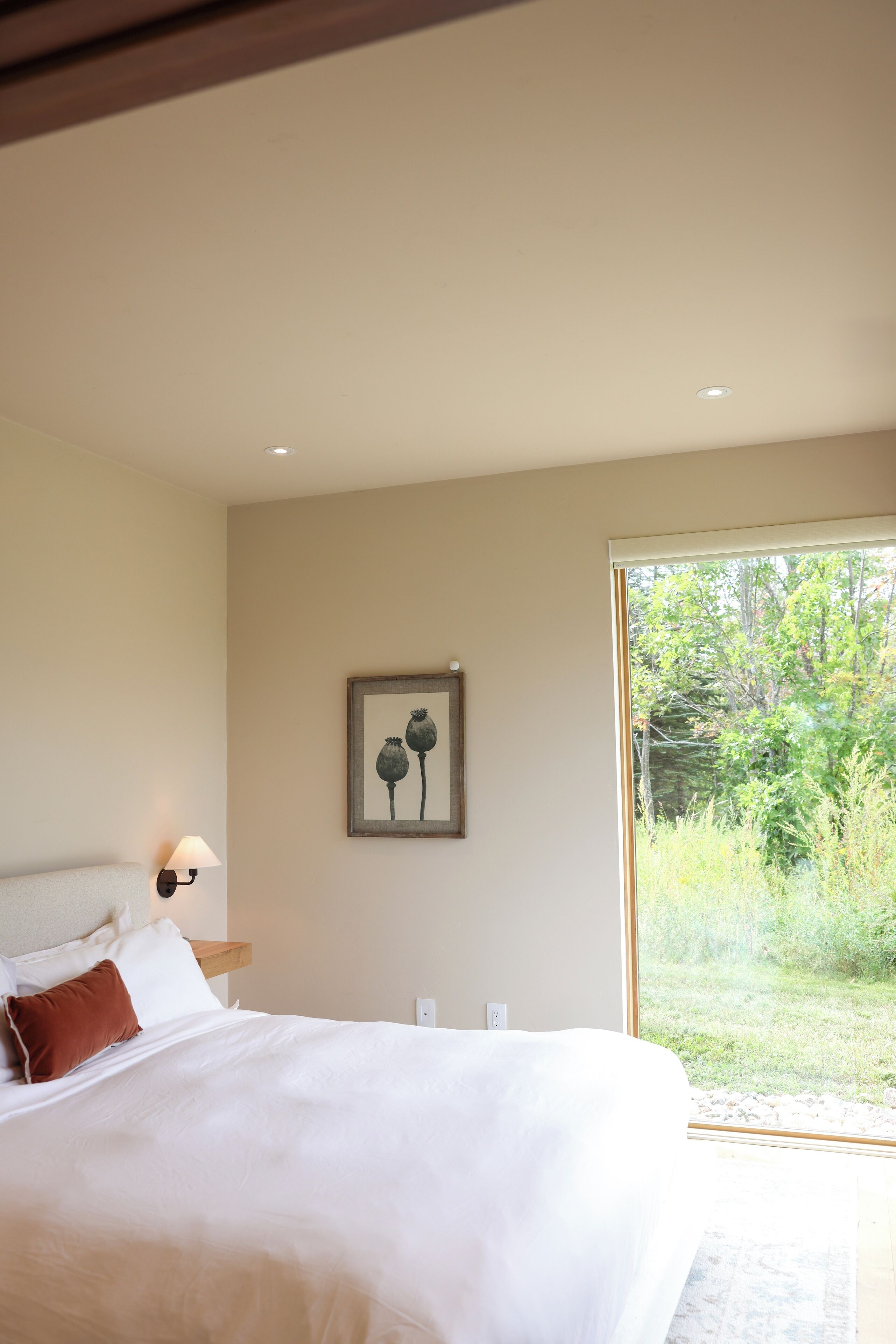Une chambre avec un grand lit, une lampe de chevet, un tableau encadré au mur et une vue sur la verdure à travers une porte vitrée.