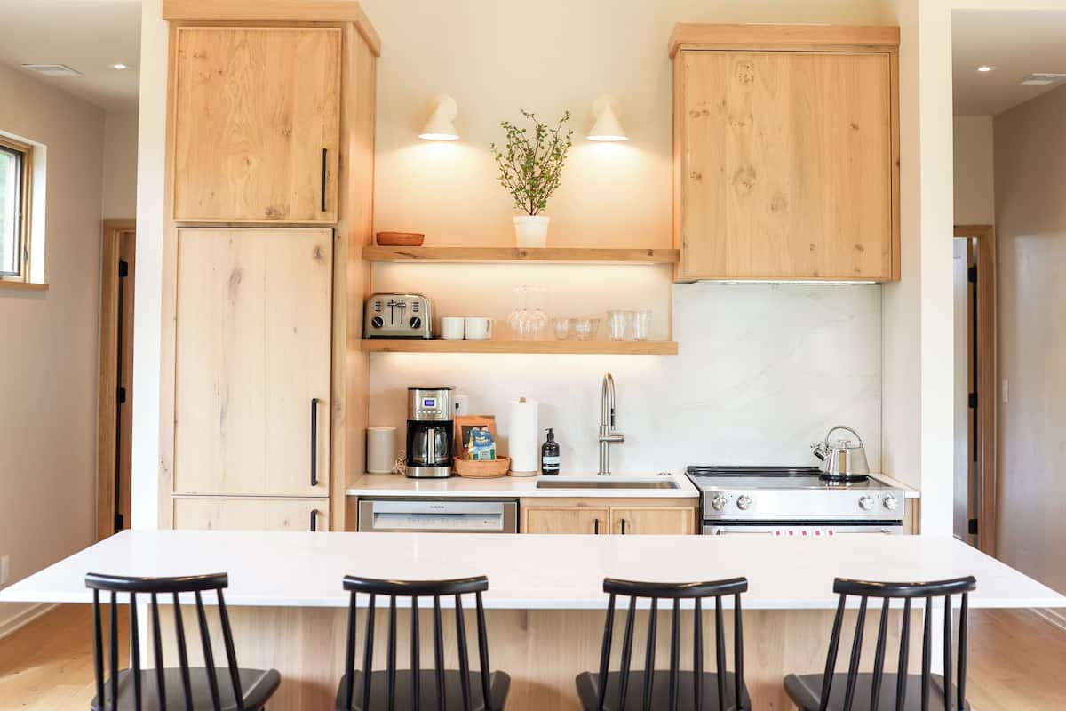 A modern kitchen with wooden cabinets, a central island with bar stools, a coffee machine, and a sink.
