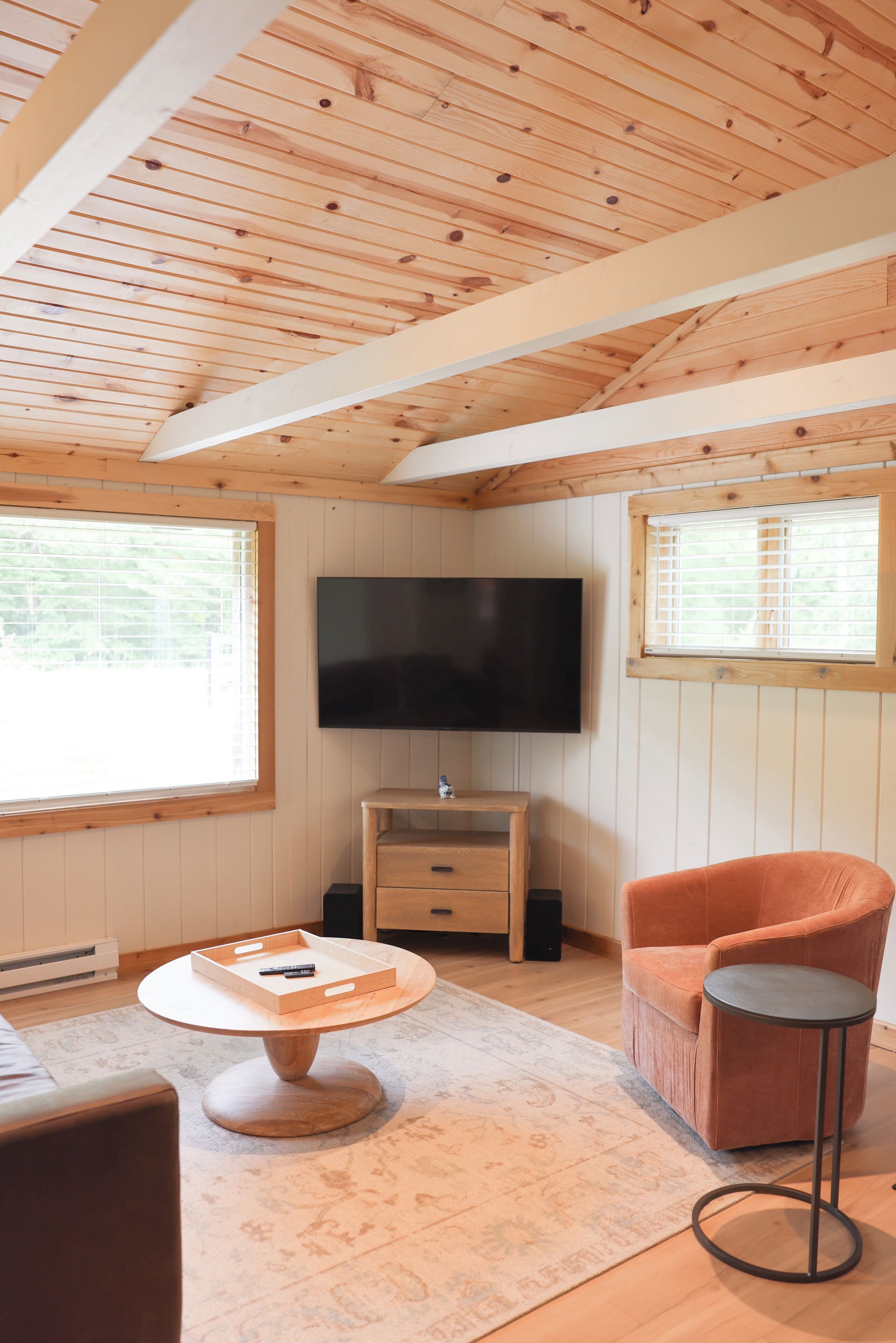 Ein gemütliches Zimmer mit Holzbalken an der Decke, einem Flachbildfernseher, einem Holztisch mit Tablett, einem gepolsterten Sessel und einem kleinen Beistelltisch.