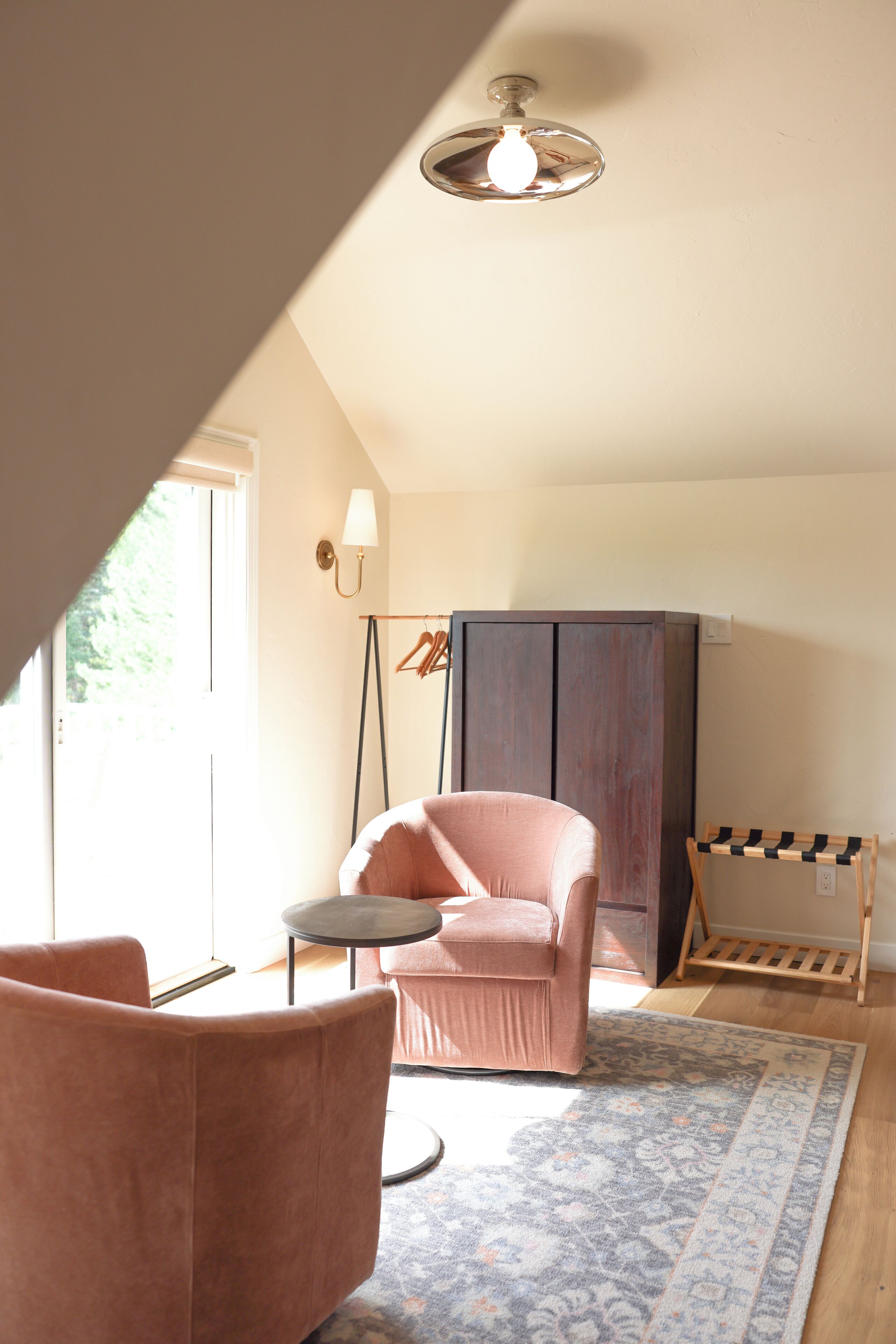 A cozy room with a pink chair, a small round table, a patterned rug, and a wardrobe.