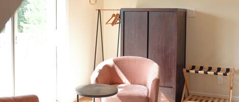 A cozy room with a pink chair, a small round table, a patterned rug, and a wardrobe.