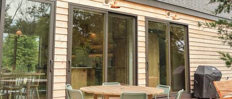 Een modern huis met een ruim terras, schuiframen en een barbecue.