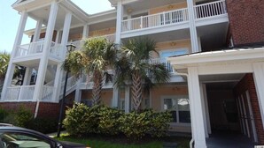 A multi-story building with balconies, a brick facade, and palm trees in the foreground. - Beautiful home in Garden City SC golf course community with easy access to beach (Murrells Inlet)