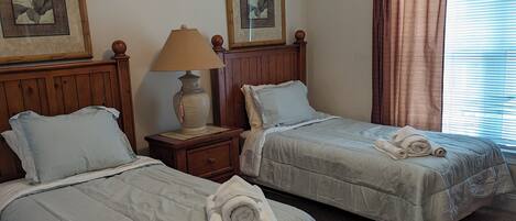 Une chambre d’hôtel avec deux lits, une table de chevet avec une lampe et deux tableaux représentant des motifs floraux, accrochés au mur.