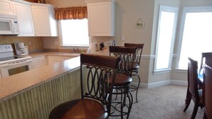 A kitchen with a bar area, white cabinets, a microwave, and a window with curtains. - Beautiful home in Garden City SC golf course community with easy access to beach (Murrells Inlet)