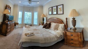 A bedroom with a large bed, wooden headboard, two bedside tables with lamps, a dresser, and a television. - Beautiful home in Garden City SC golf course community with easy access to beach (Murrells Inlet)