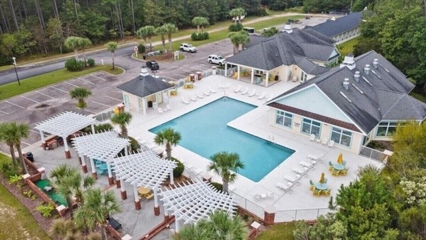 A resort with a large swimming pool, covered outdoor seating areas, and a building with multiple windows. - Beautiful home in Garden City SC golf course community with easy access to beach (Murrells Inlet)
