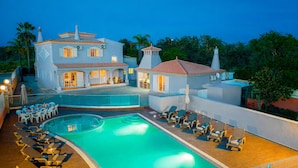 A large building with a swimming pool, lounge chairs, and a covered patio area.