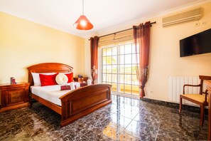 A bedroom with a bed, a nightstand, a chair, a television, and a window with curtains.