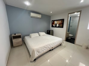 A bedroom with a bed, bedside table, and an air conditioning unit. - Lagos Apartaestudios x2 (Barranquilla)