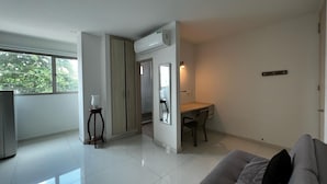 A modern living room with a sofa, a dining area with a table and chairs, a TV, and a large window with a view of trees.