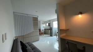 A modern living room with a grey sofa, a dining area with a wooden table and chairs, a kitchen with white cabinets, and a small island with a sink.