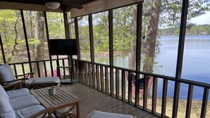 Una terraza techada con mobiliario de madera, un televisor de pantalla plana y vistas a un lago.