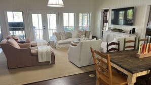 Una sala de estar acogedora con un sofá, una mesita de centro y una mesa de comedor con sillas. Hay un televisor montado en la pared y una ventana con vistas al exterior.