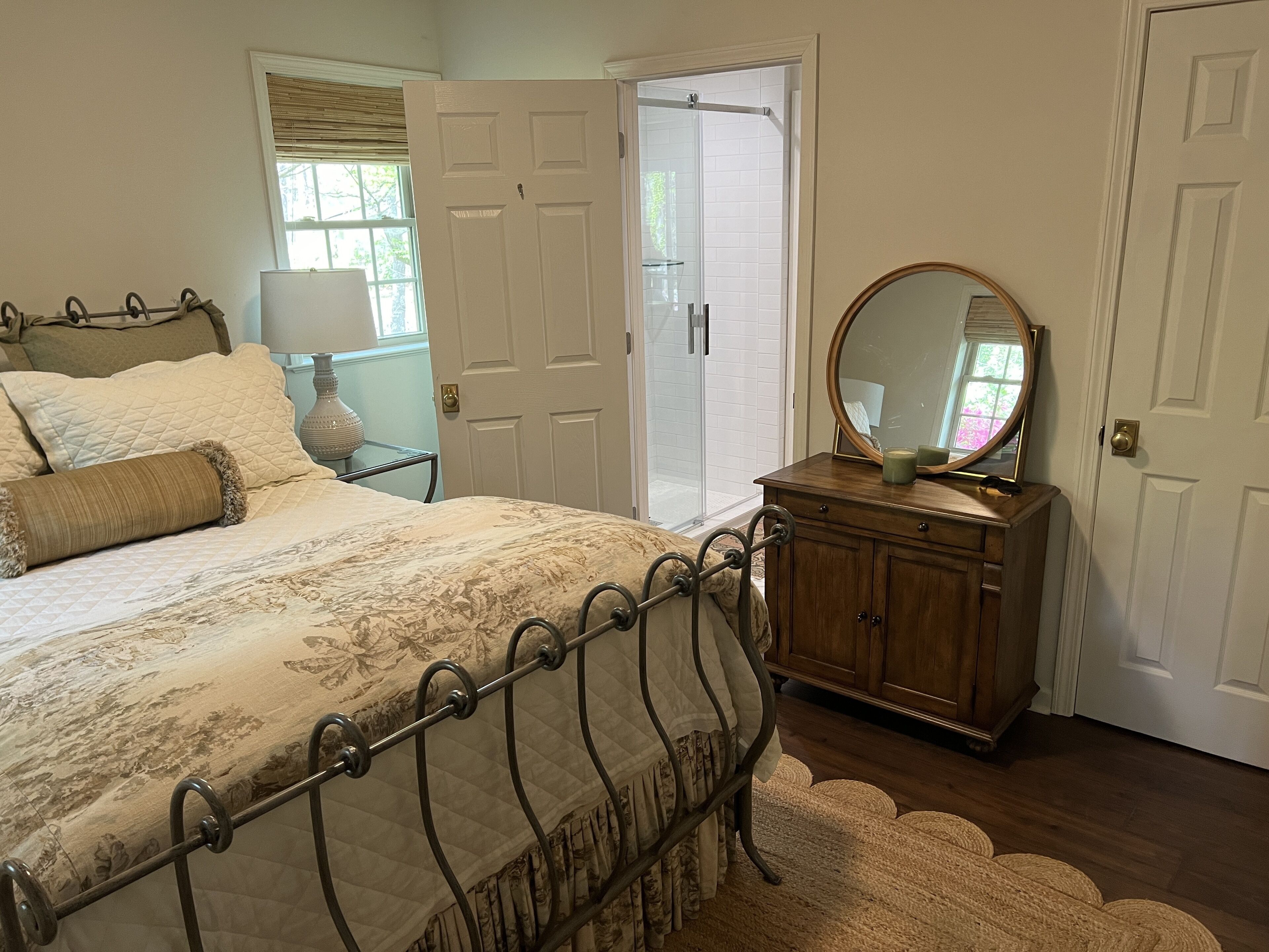 A bedroom with a bed, a wooden dresser, a mirror, and a door leading to a bathroom.