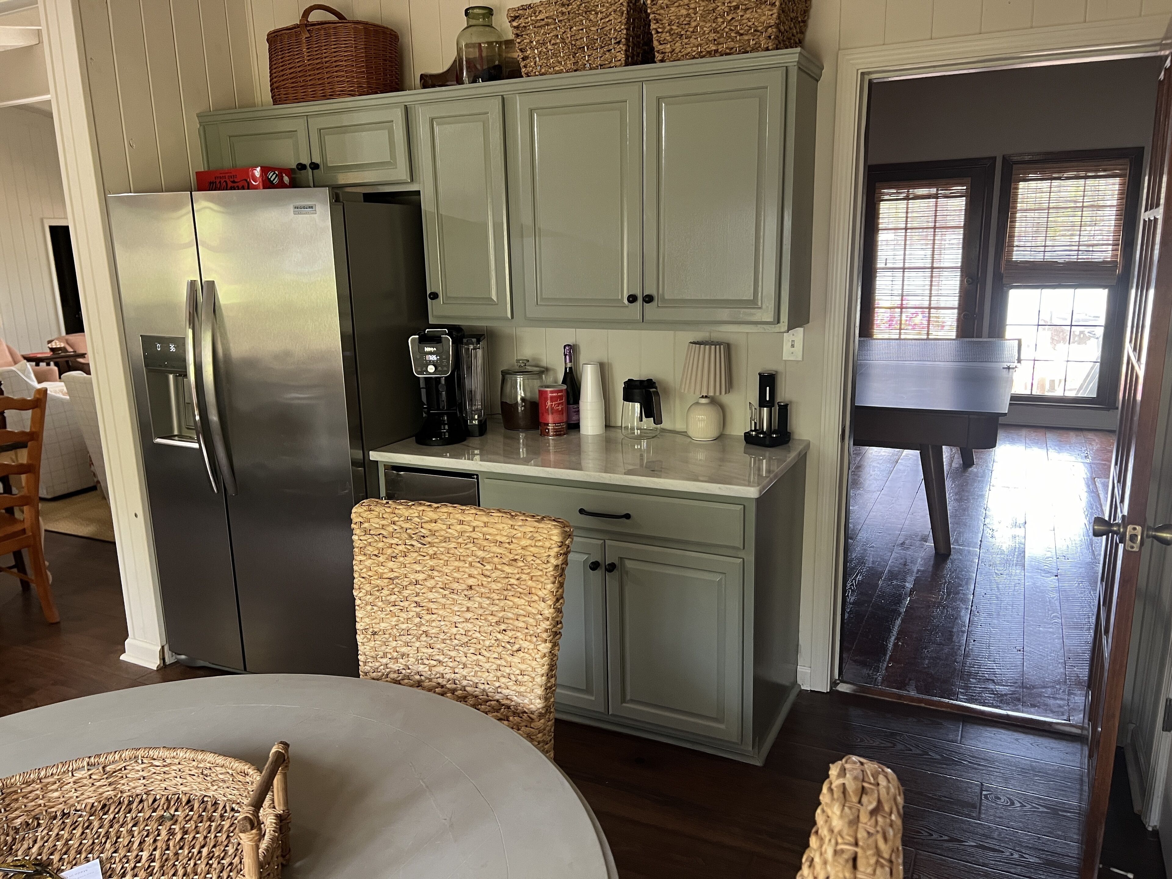 A kitchen with a refrigerator, coffee maker, and wicker baskets on the counter.