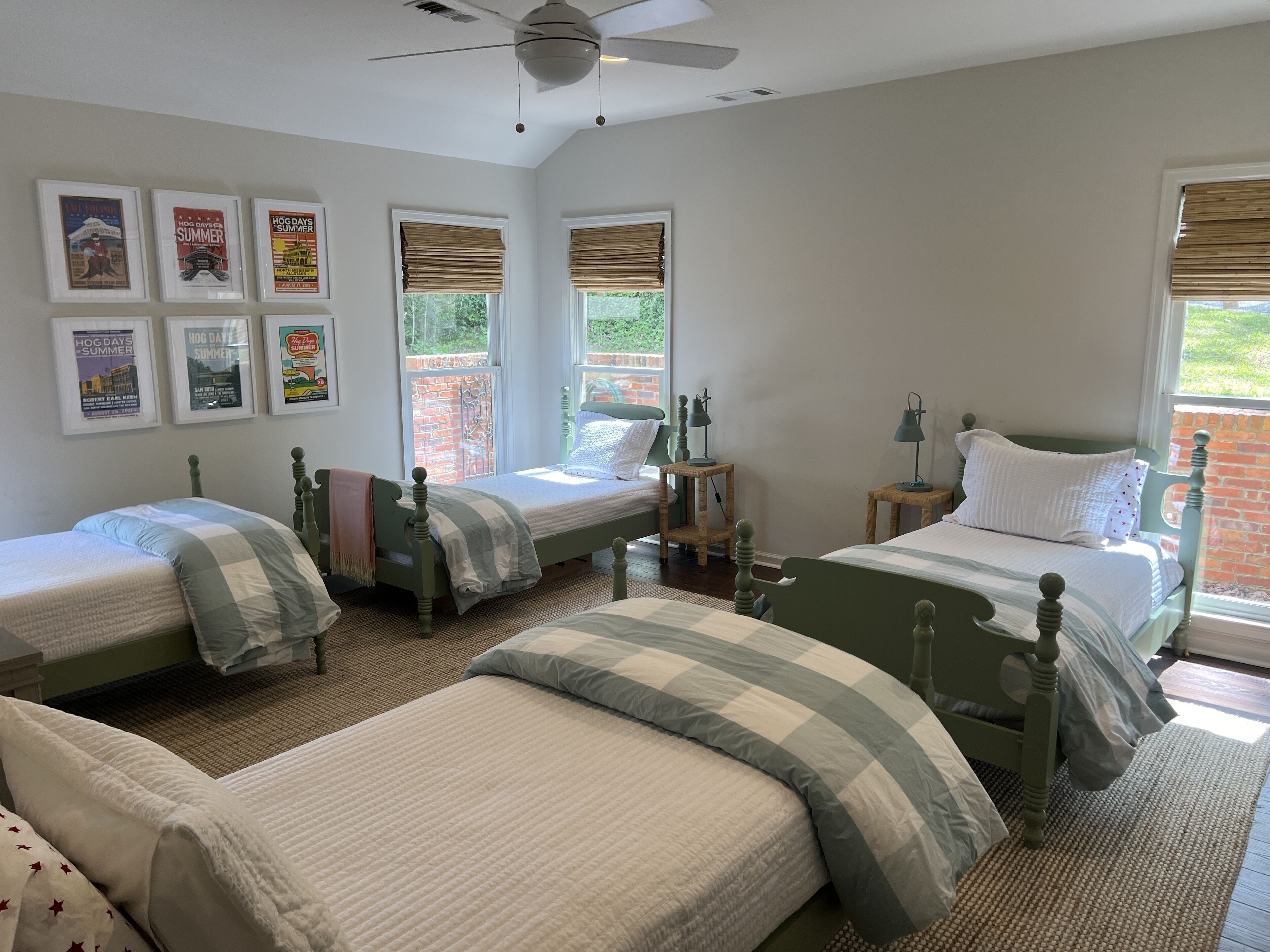 A bedroom with three single beds, a ceiling fan, and large windows with blinds.