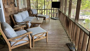 Una terraza de madera con mobiliario exterior, incluyendo sofás y una mesa, y vistas a una zona boscosa.