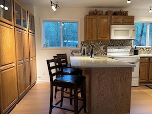 A kitchen with wooden cabinets, a large island with bar stools, a microwave, and a view of trees through the window.