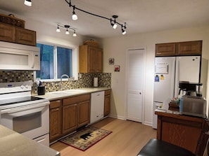 Una cocina con armarios de madera, microondas, estufa, refrigerador y cafetera.
