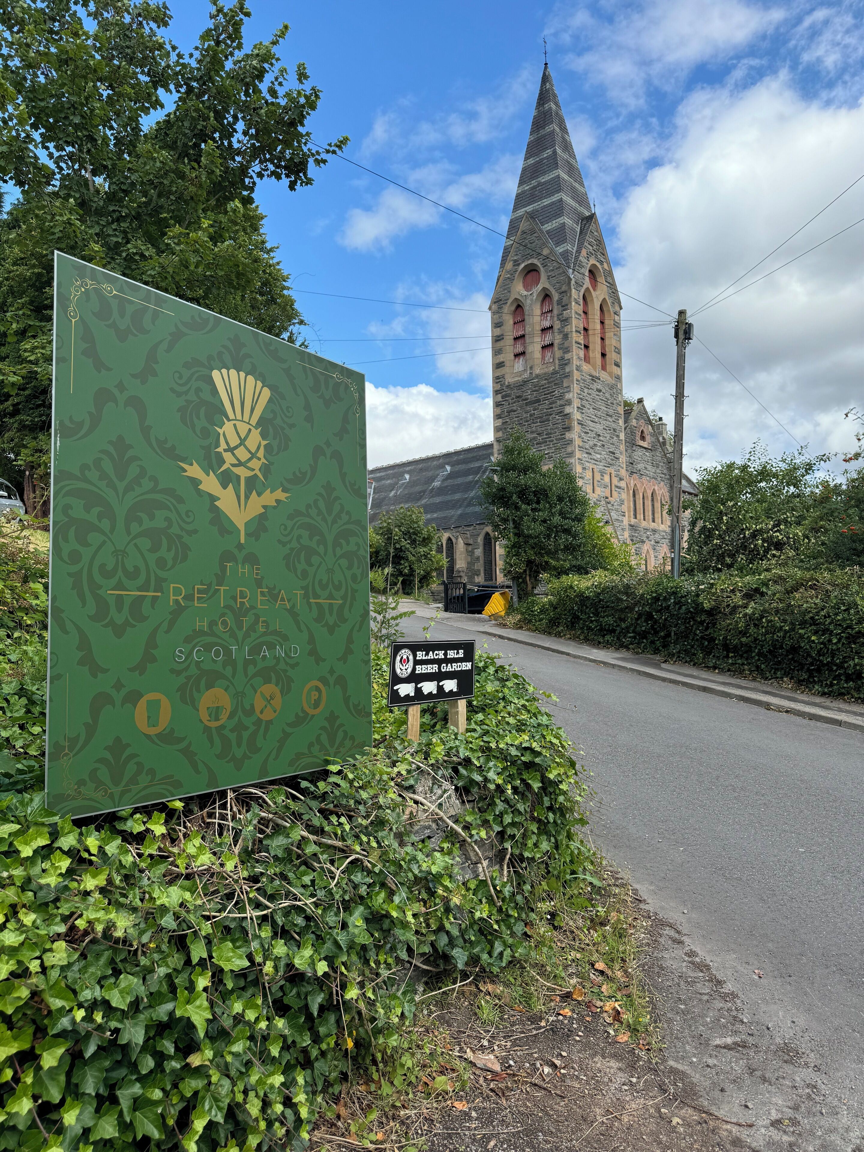 A sign for The Retreat Hotel in Scotland, a stone building with a pointed tower, and a sign for Black Isle Elder Garden.