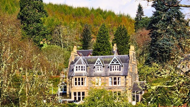 A historic stone building with multiple chimneys, surrounded by dense foliage and trees. - The Retreat Hotel  (Strathpeffer)