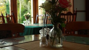 A dining table with a clear glass vase containing flowers, salt and pepper shakers, and a fork and knife set. - The Retreat Hotel  (Strathpeffer)
