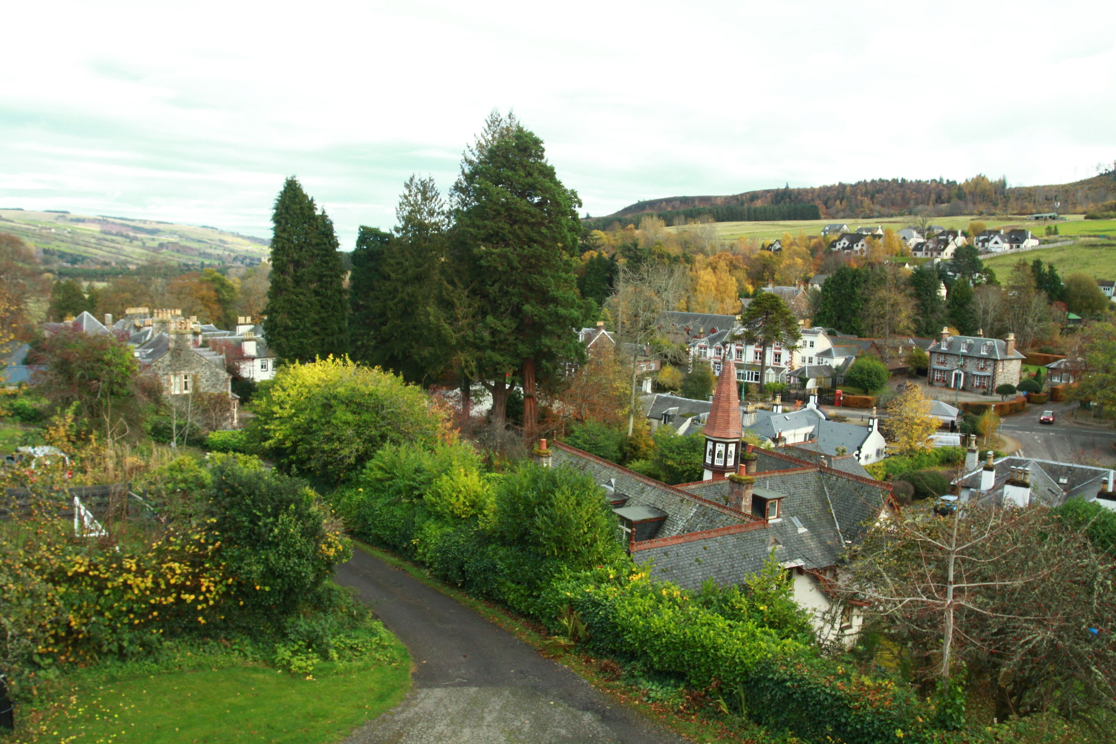 A village with traditional architecture, including a prominent church steeple, surrounded by lush greenery and a winding road.