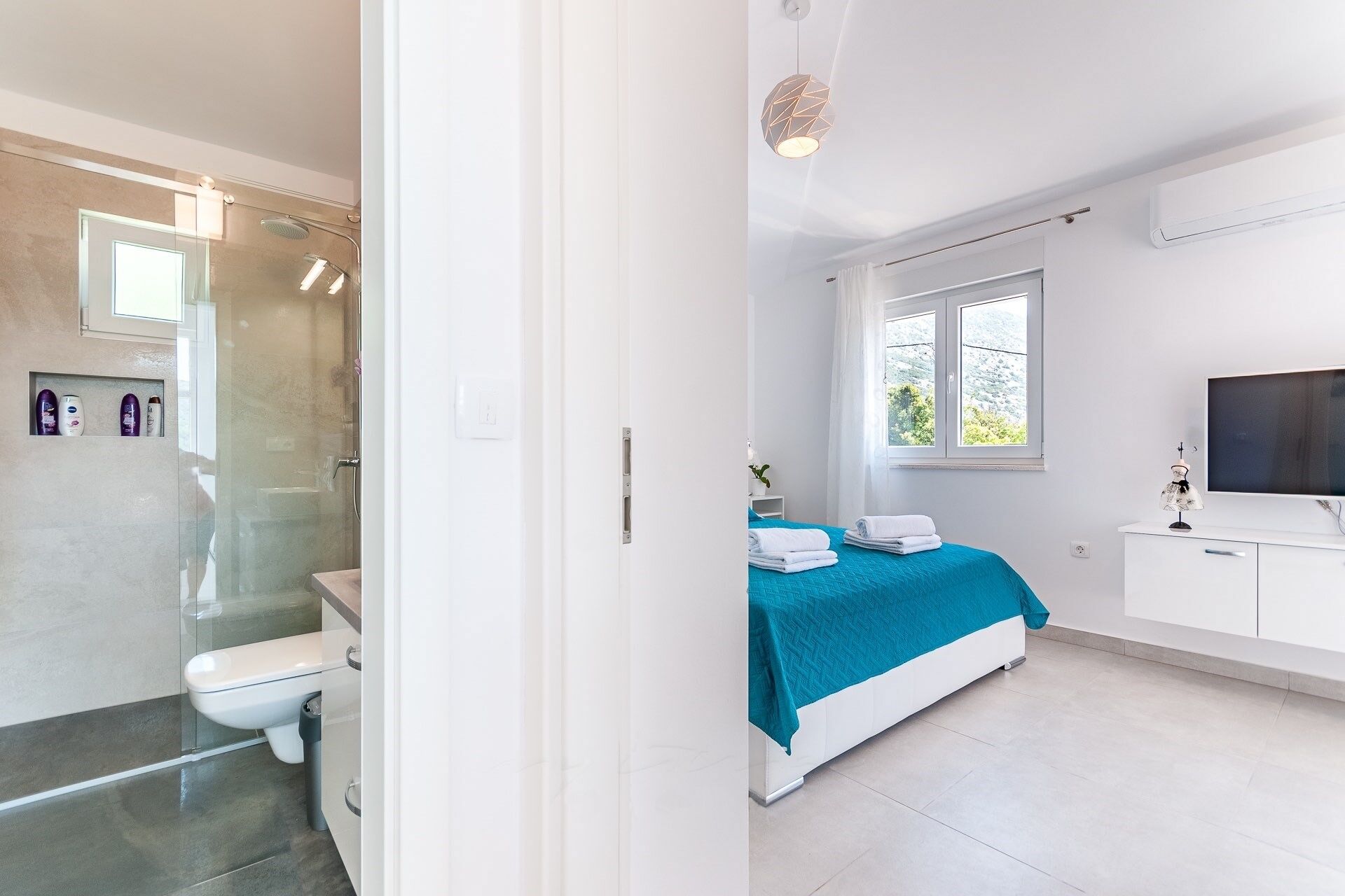 A modern bedroom with a bed, a TV, and a bathroom with a shower and toilet.