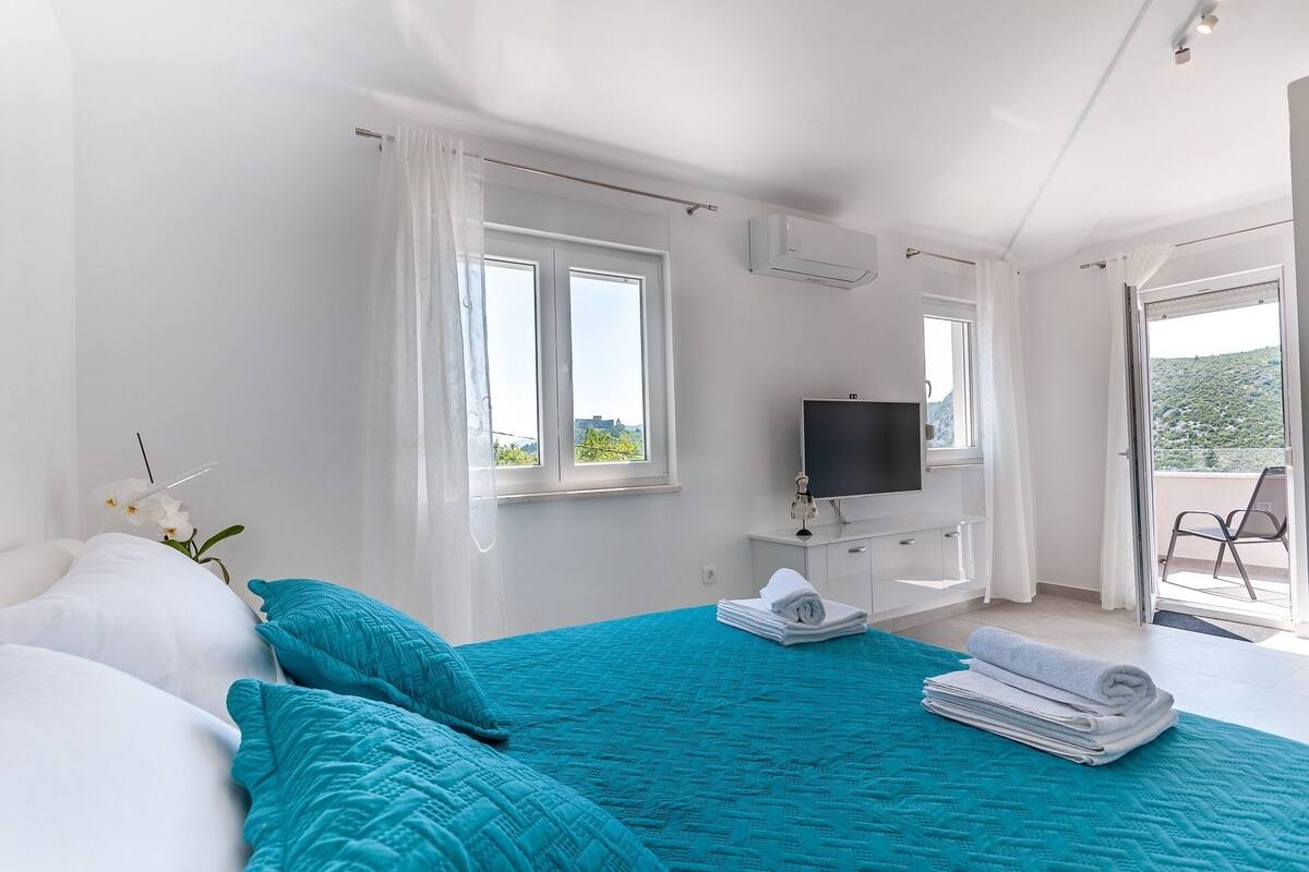 Une chambre à coucher avec un lit, une télévision et un balcon équipé d’une chaise.