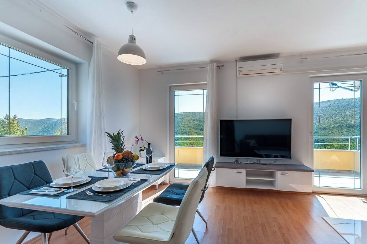Un salon moderne avec un coin repas, de grandes fenêtres et un téléviseur.