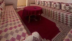 Een kamer met een gestreept bankstel, een ronde tafel met een rode tafelkleed en een plafond met blauwe en rode verlichting.