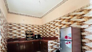 Een kleine keuken met behang, donkerhouten kastjes en een roestvrijstalen koelkast.