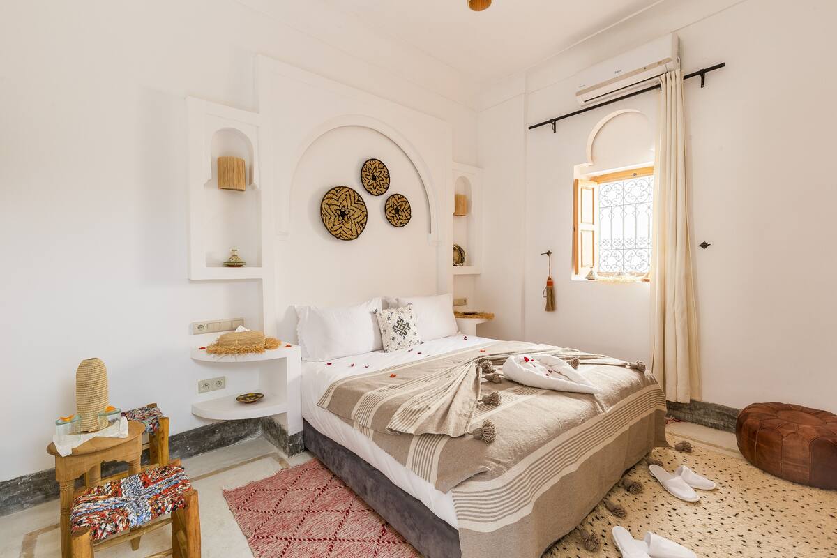A bedroom with a large bed, a wooden bench, a red rug, and decorative wall art.
