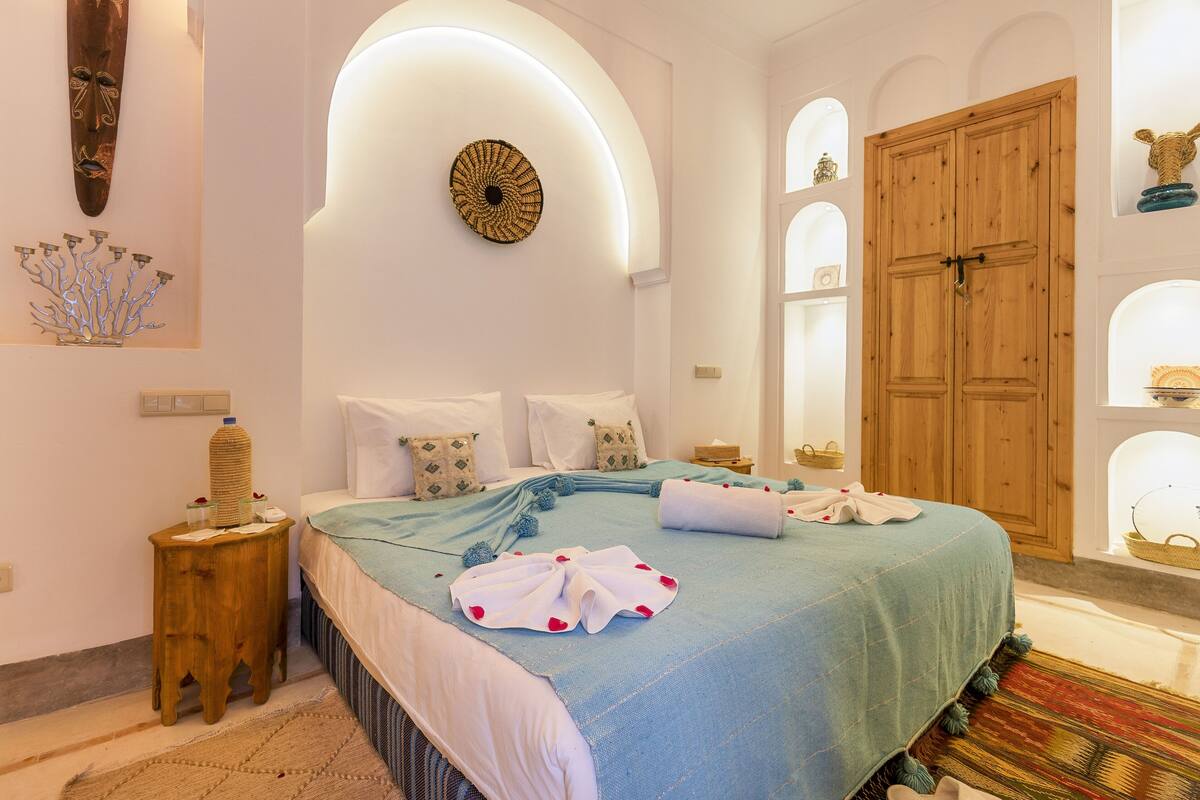 A bedroom with a bed, wooden wardrobe, and decorative wall art.