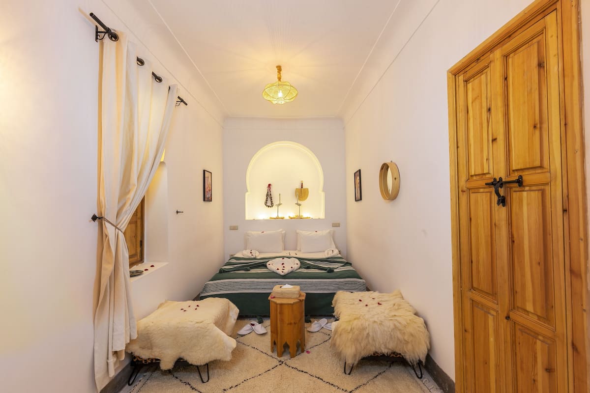 A narrow hallway leading to a bedroom with a bed, a wooden wardrobe, and a small stool.